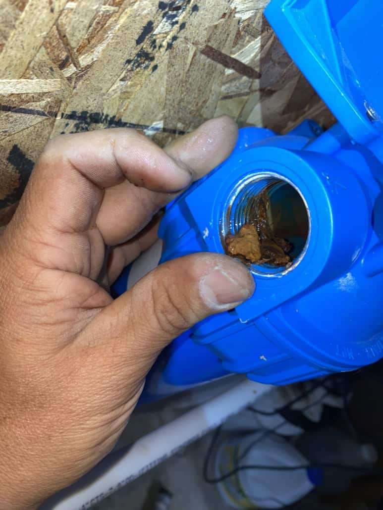 A plumber holds open the filter housing inlet to show the rust and corrosion built up inside the threads after the old fittings came off