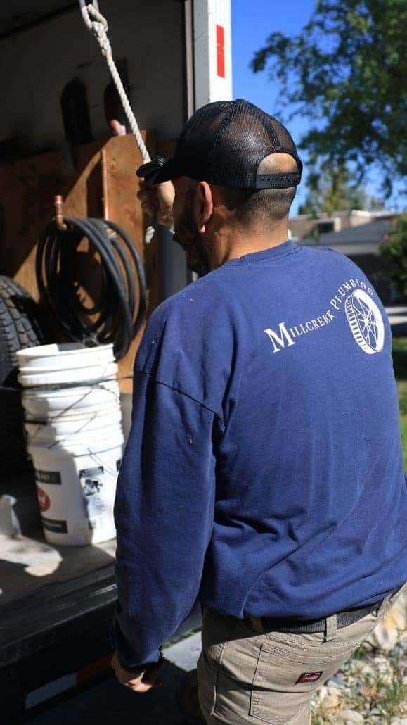 Millcreek Plumbing Technician Unloading Equipment from Trailer Millcreek Plumbing technician in a company shirt pulling equipment from a work trailer stocked with hoses and buckets