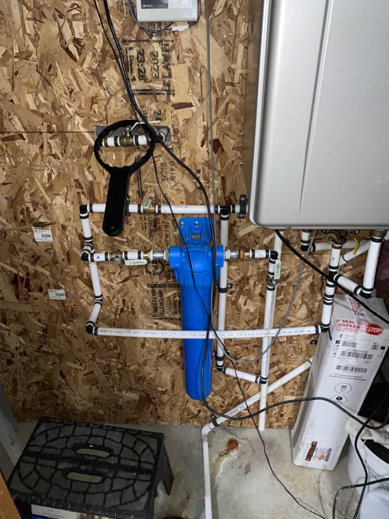 The whole-house filter reconnected with new copper and brass fittings, with the old corroded steel nipples on the floor below